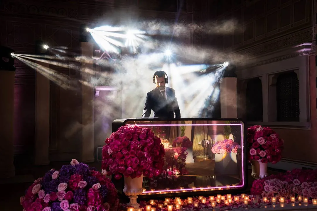 Sala da ballo in penombra con fasci di luce, consolle specchiata, rose e candele durante un evento privato a Firenze